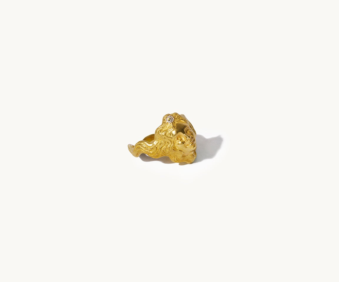 An 18K yellow gold ring resembling a small face, with a tiny diamond set in her hair, which forms the ring's shank.