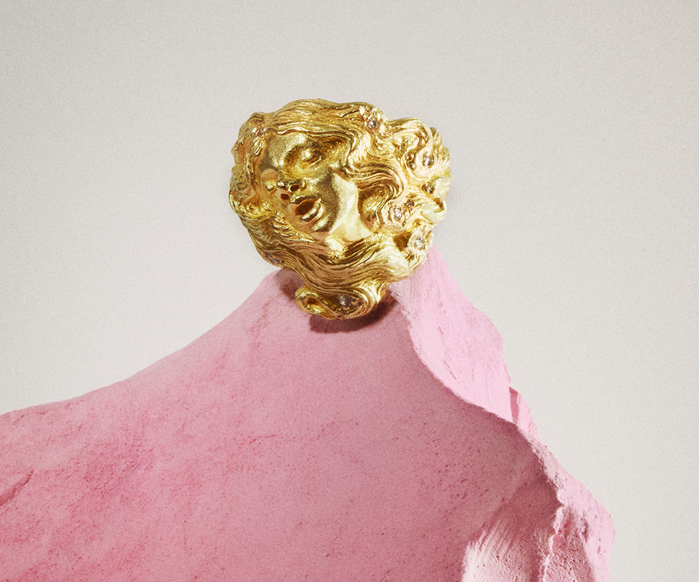An 18K yellow gold ring with small diamonds, organically shaped to resemble a woman, with her hair seamlessly integrated into the design.