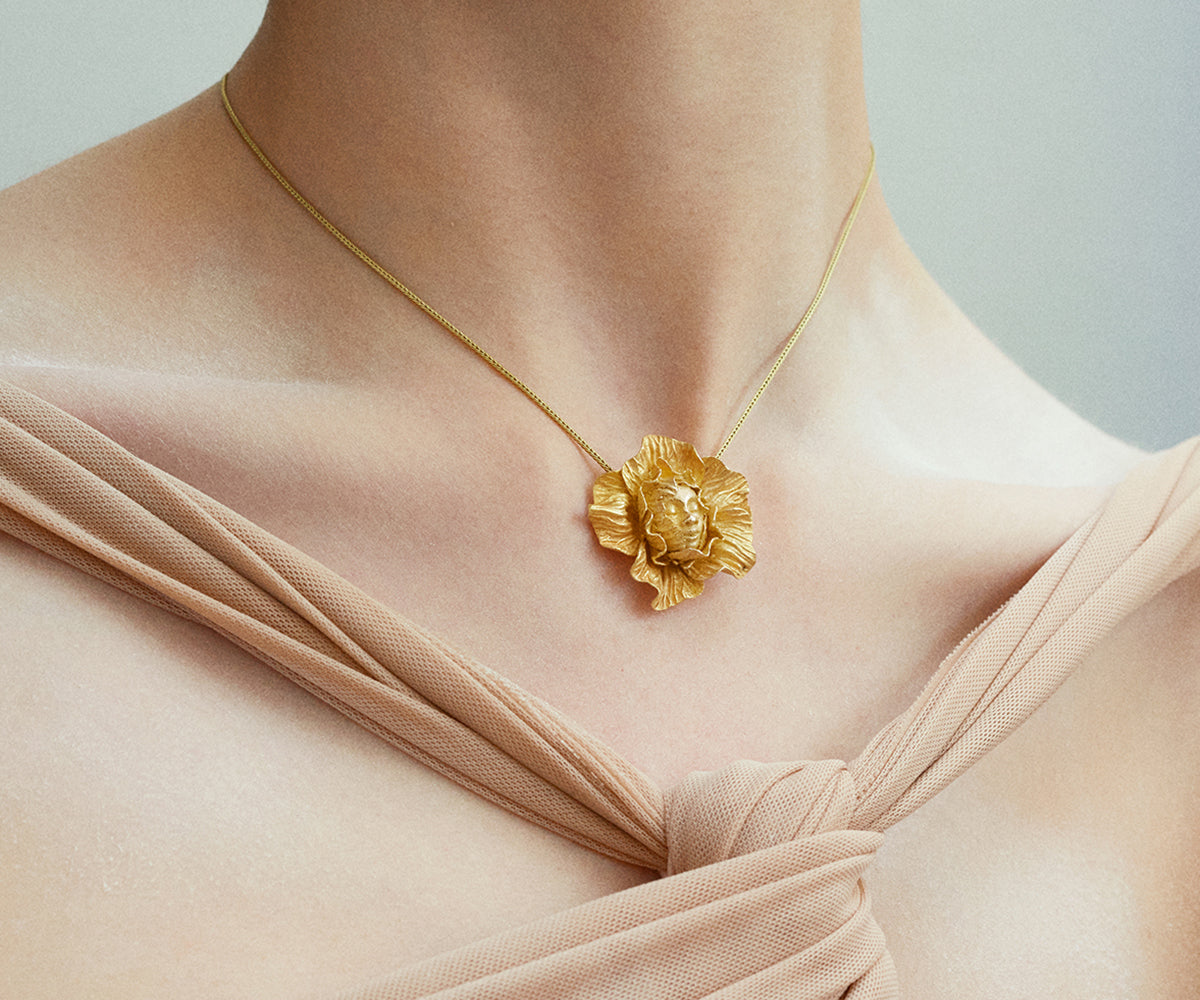 An 18K yellow gold necklace with a pendant shaped like a face lurking among leaves.