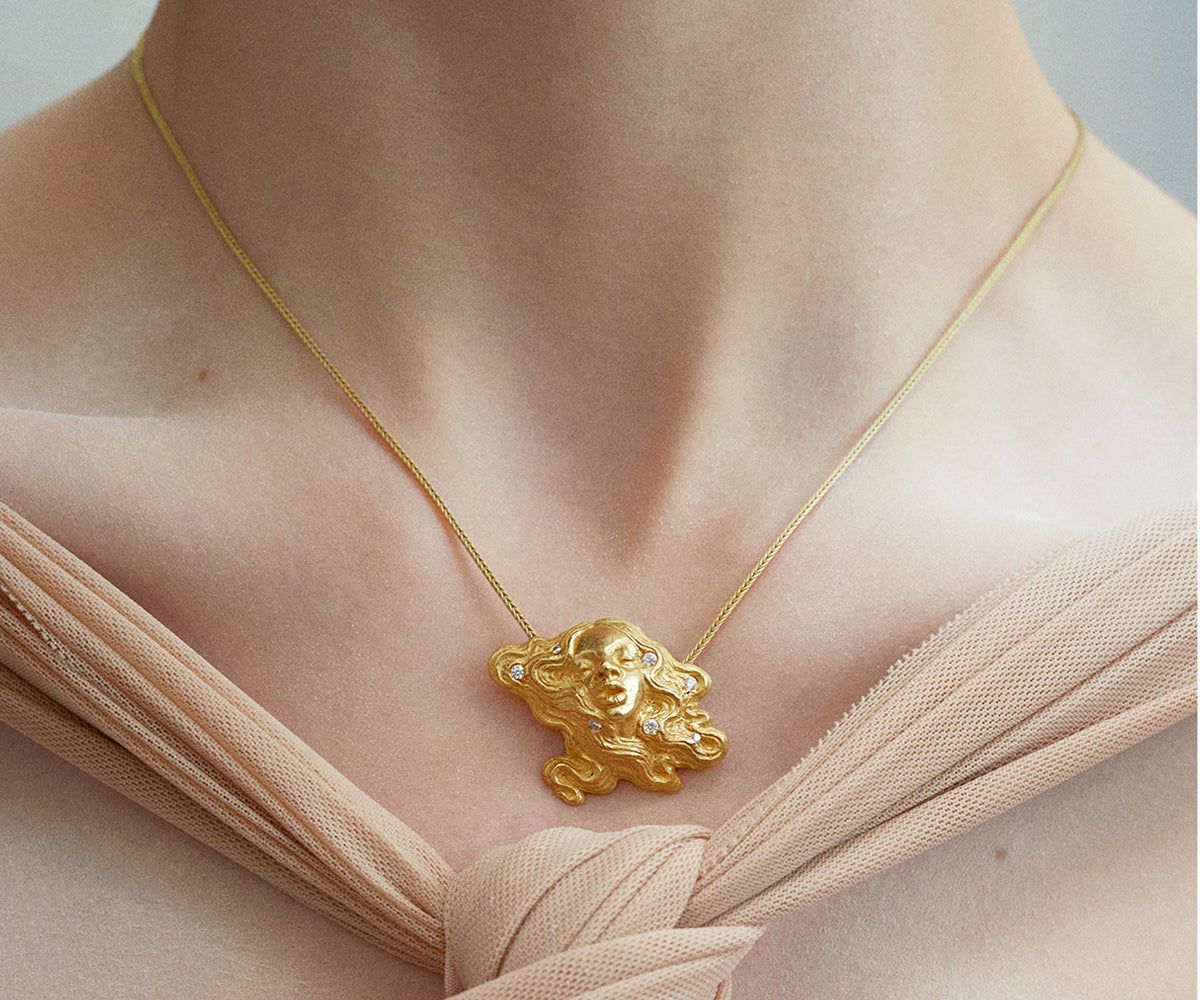 An 18K yellow gold necklace with a pendant looking with a woman with loose hair. 7 diamonds are placed finely in her hair.
