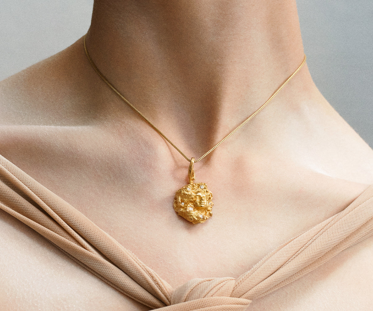 An 18K yellow gold necklace with a pendant shaped like a woman, emerging from between the branches of an oak tree. Small diamonds appear in the surface.