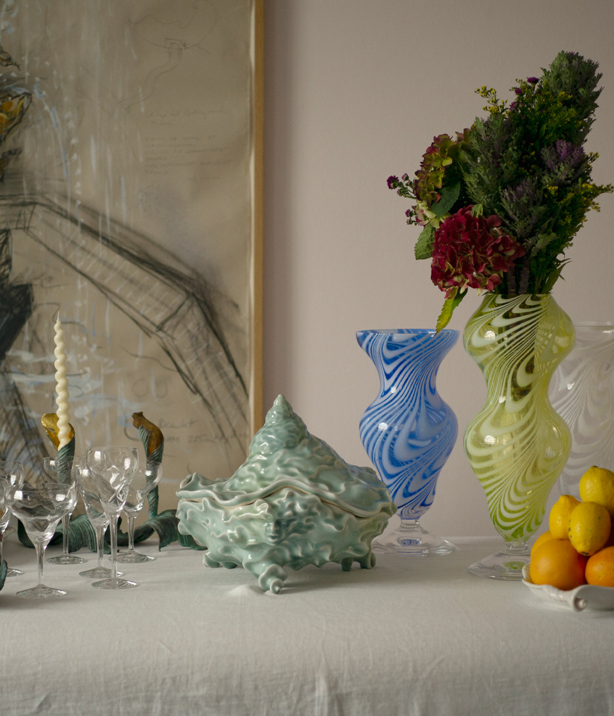 A table set with glasses, a sea tureen and glass vases. One of them filled with flowers.