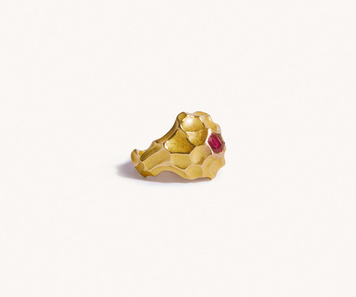 A large, wave-shaped 18K yellow gold ring with a centered round ruby, set against a white background.