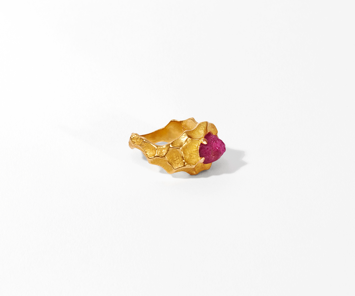 18K yellow gold ring featuring a rough, unpolished ruby at its center, with the surface designed to resemble waves.