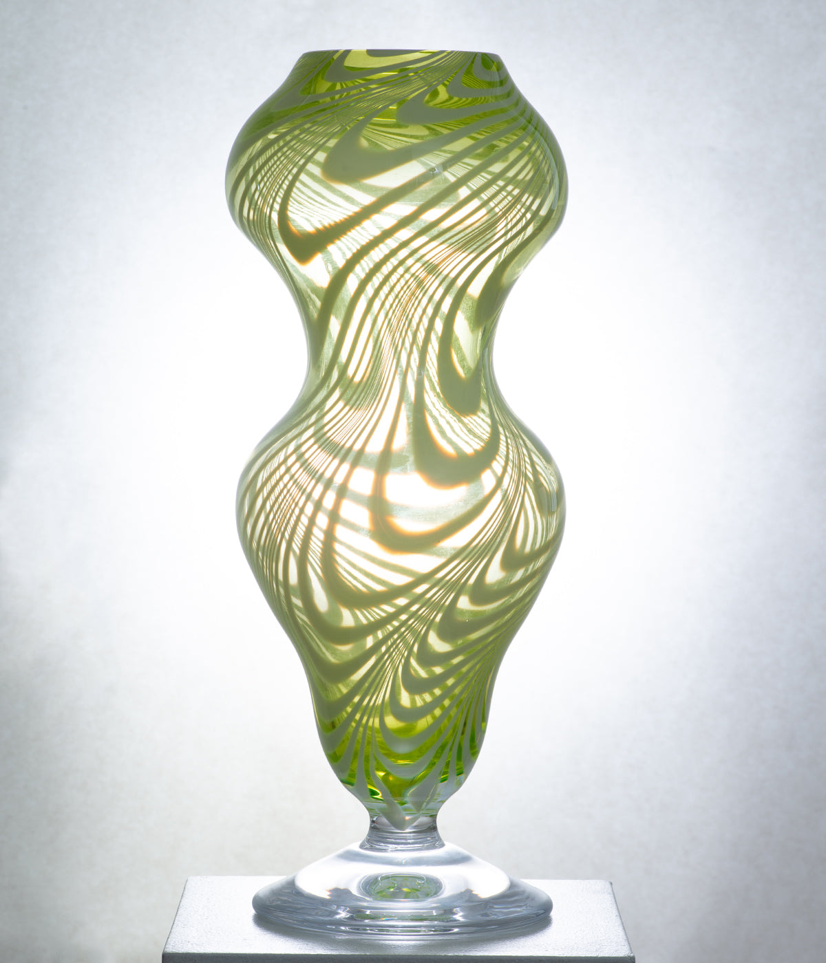 A unique mouth-blown glass vessel with green and organic white stripes, featuring a swirling, almost liquid-like see-through design.
