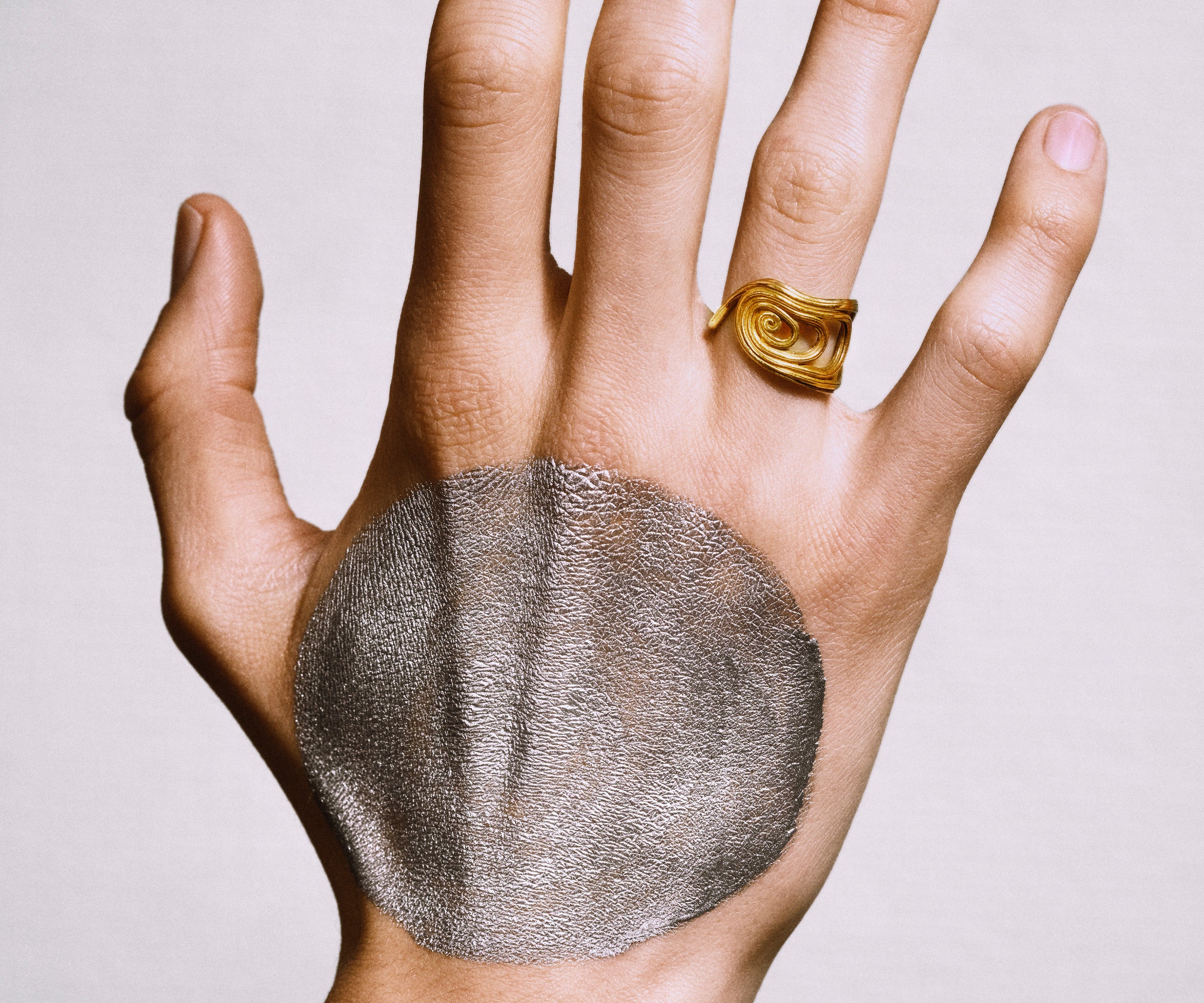 A male hand wearing an 18K yellow gold ring designed to resemble a large fan.