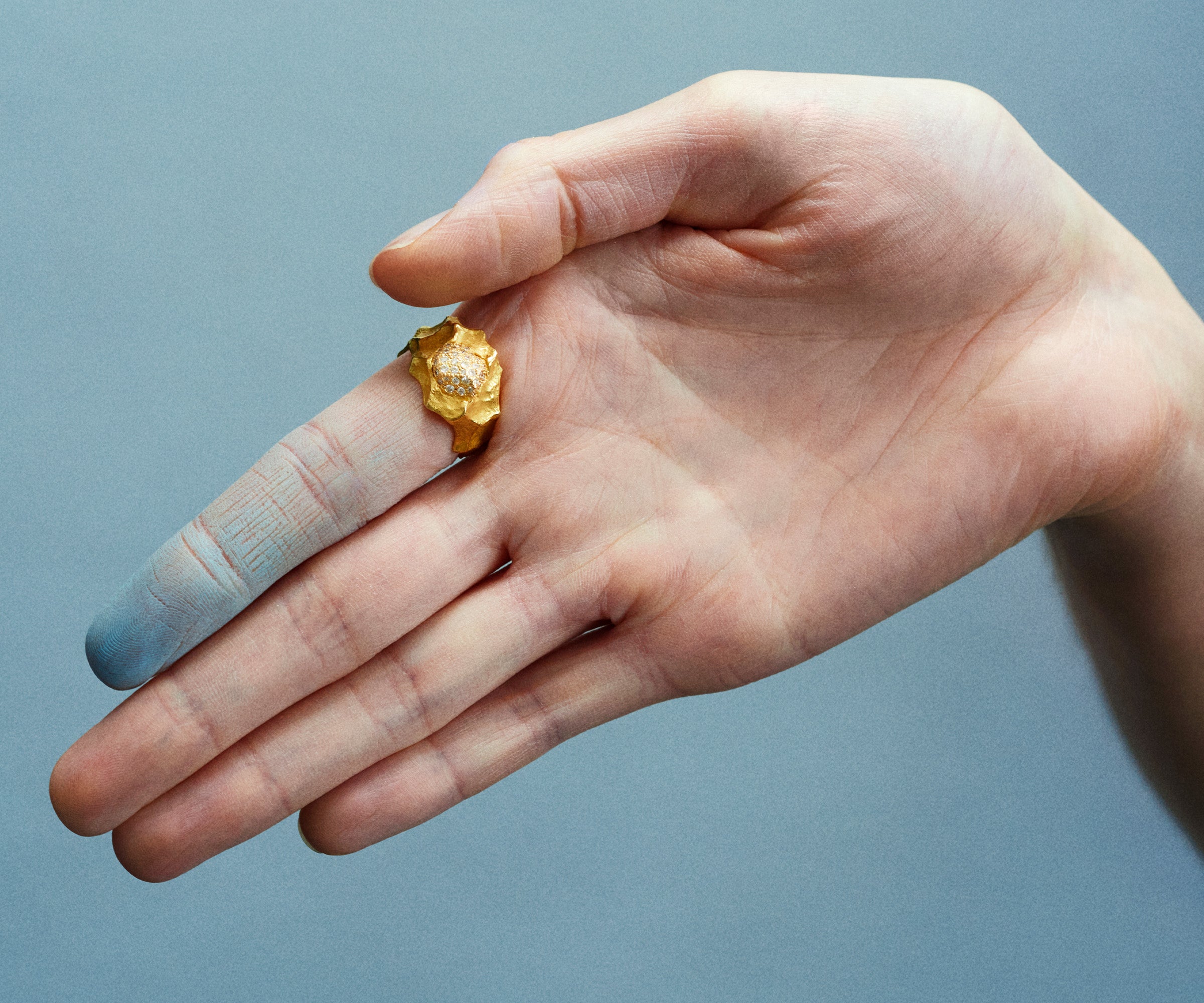 A stunning 18K yellow gold ring worn on a hand, designed to resemble ocean waves, adorned with 20 small diamonds set in the center.