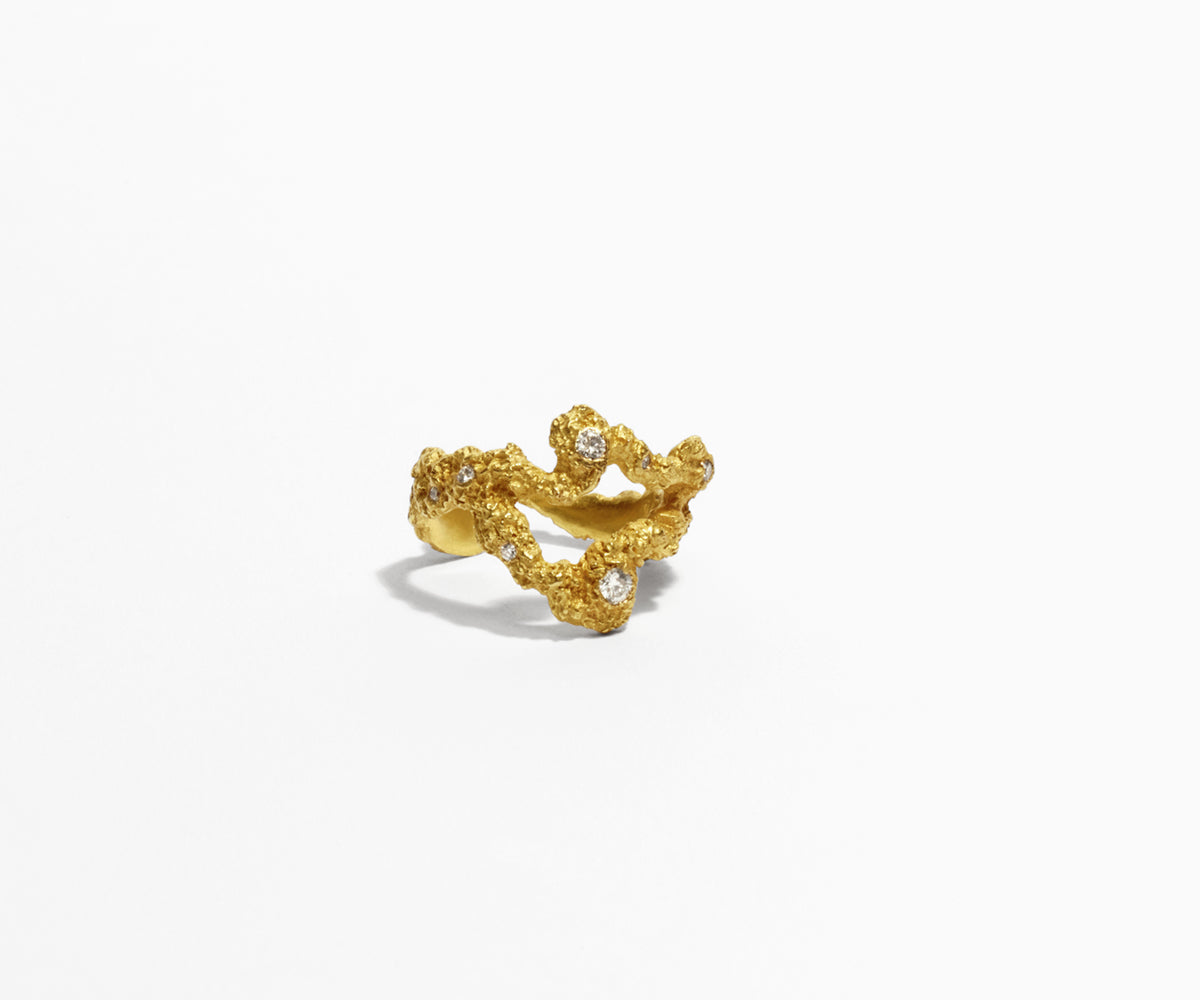 An 18K yellow gold ring with 13 small diamonds, shaped organically with a whole in the middle in front. The surface of the gold resembles craters.