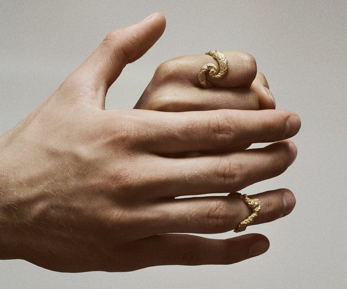 Two hands wearing 18K yellow gold rings with 7 small diamonds, shaped organically, inspired by the universe.