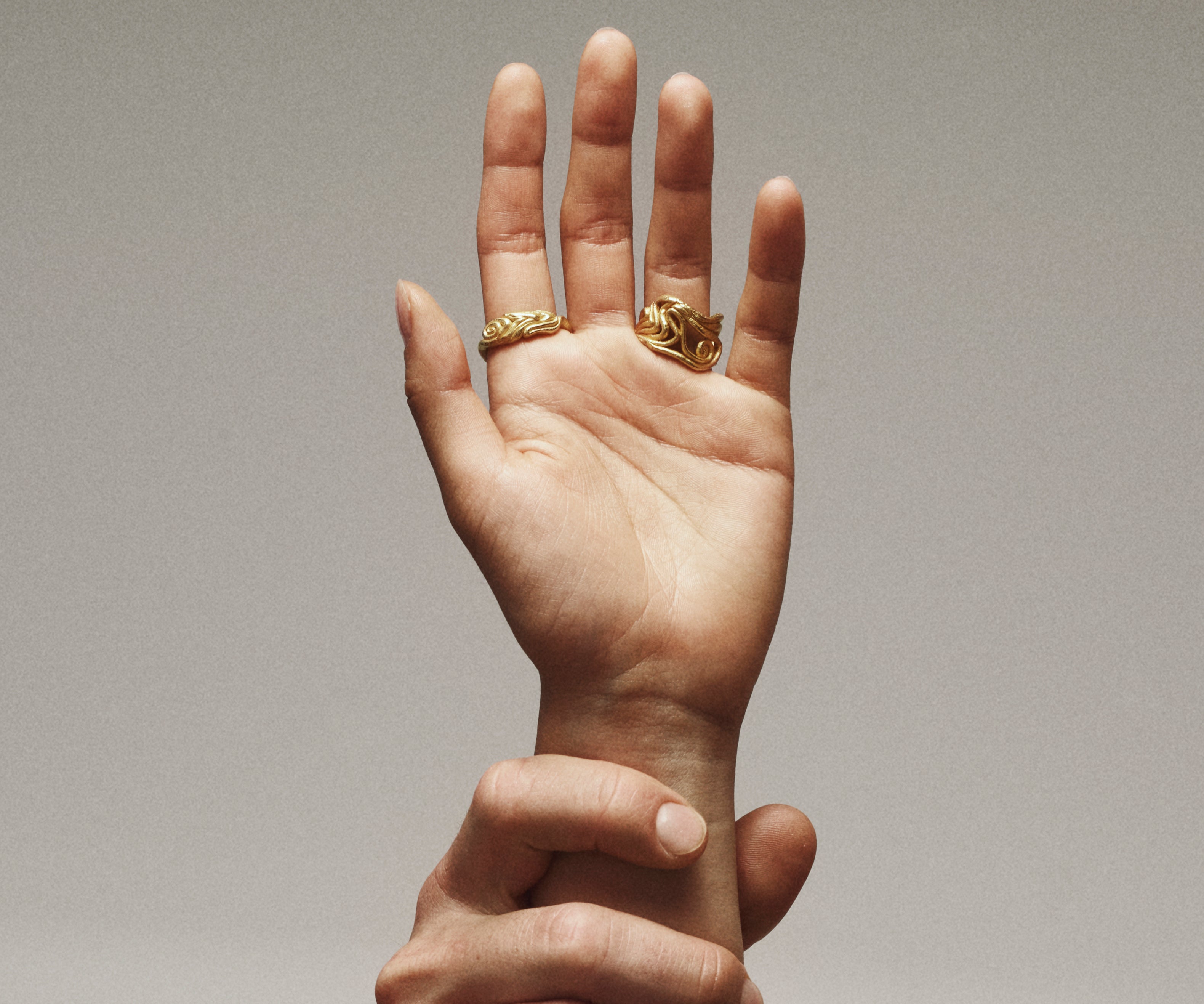 A hand wearing 2 rings in 18K yellow gold, shaped organically, inspired by nature.