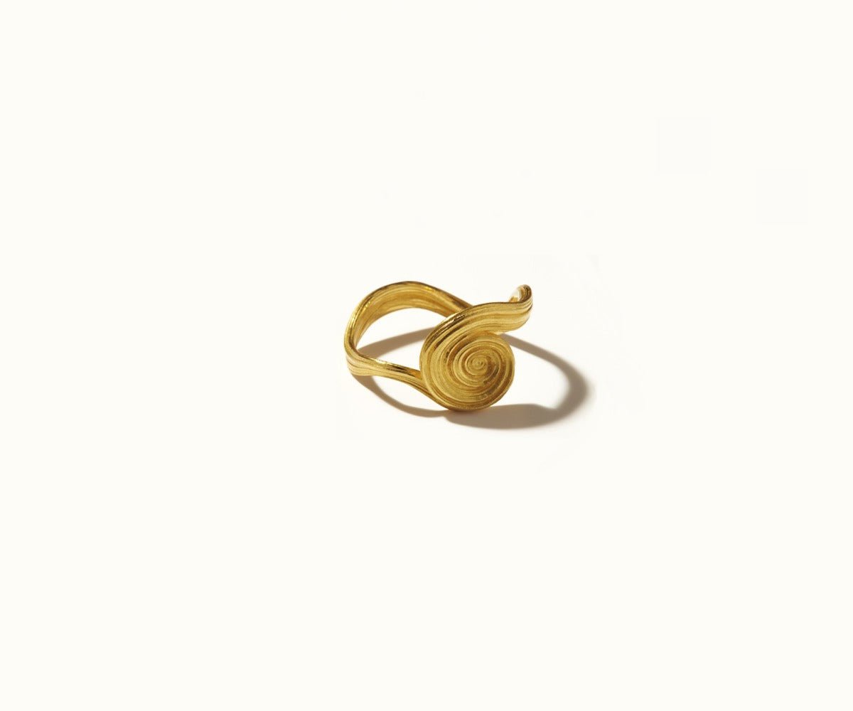 A spiral-shaped ring in 18K yellow gold, featuring an organic form, set against a white background.